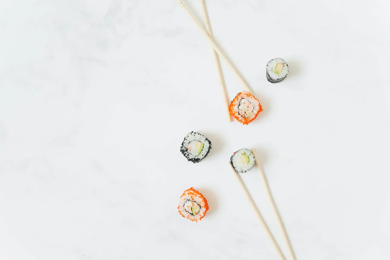 sushi 5Different types of mini sushi rolls placed on a white background, paired with chopsticks